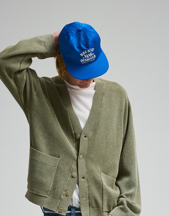 A young man poses in a photography studio wearing a bay leaf green Bayview Acid Wash Cardigan Sweater.