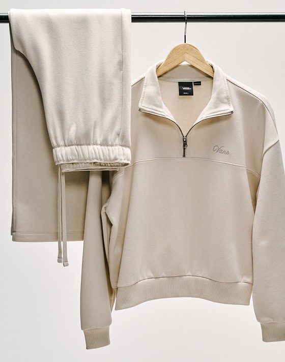 The taupe mist gray Script Logo Mock Neck Sweatshirt hangs from a rack in a photography studio.