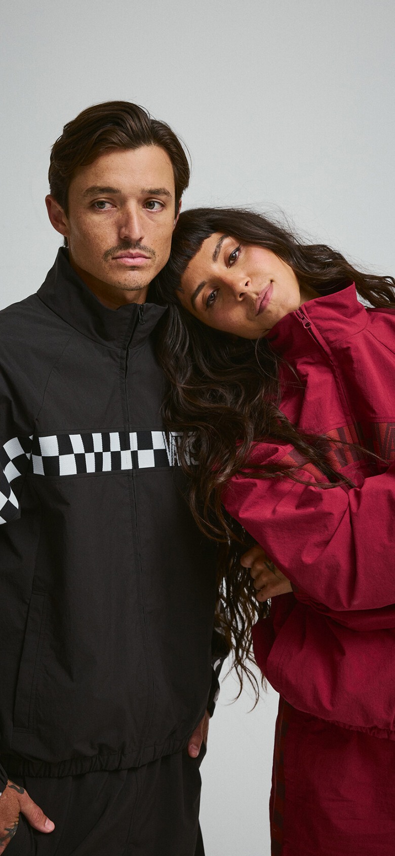 A young man and woman pose in black and red Ronnie Track Jackets and Ronnie Track pants in a photography studio.