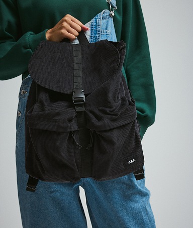 A close-up of someone holding the black Scatter Backpack against the blue denim Sirelle overalls in a photography studio.