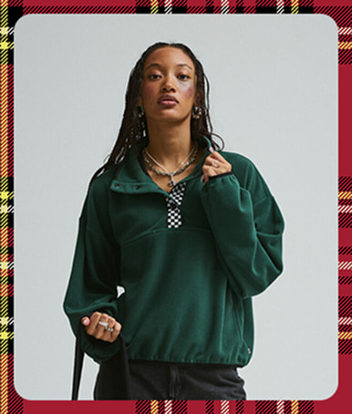 A young woman poses in a photography studio in a green Script Logo Mock Neck Sweatshirt.