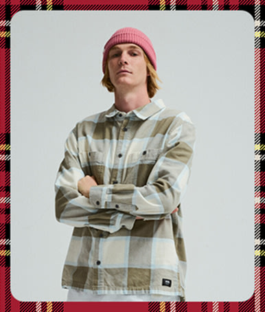 A young man crosses his arm and poses in a photography studio wearing a turtledove white Larkspur Plaid Flannel Shirt.