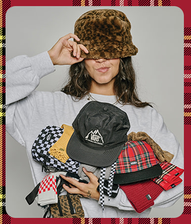 Une jeune femme pose dans un studio photo, portant un chapeau bob à imprimé léopard et tenant plusieurs paires de chaussettes et casquettes Vans.