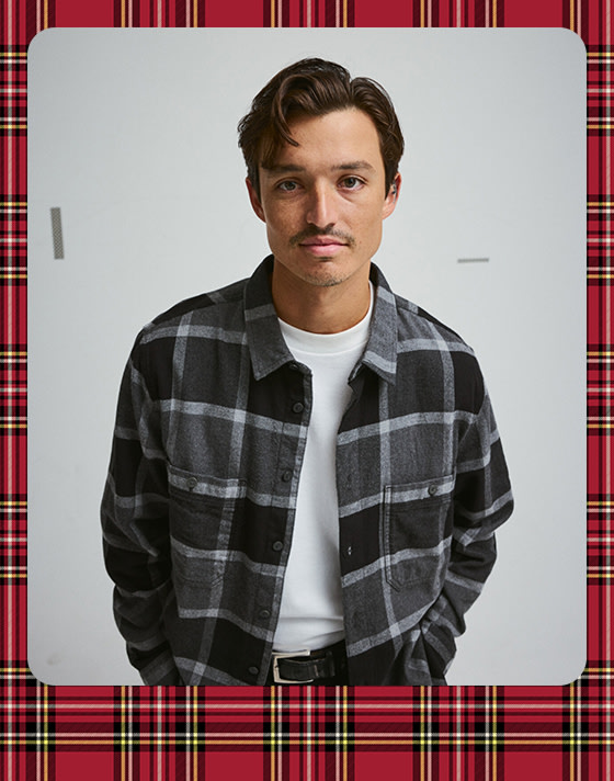 Une photographie entourée d'une bordure de vacances à carreaux d'un jeune homme portant la chemise Larkspur Plaid Flannel gris brumeux asphalté.