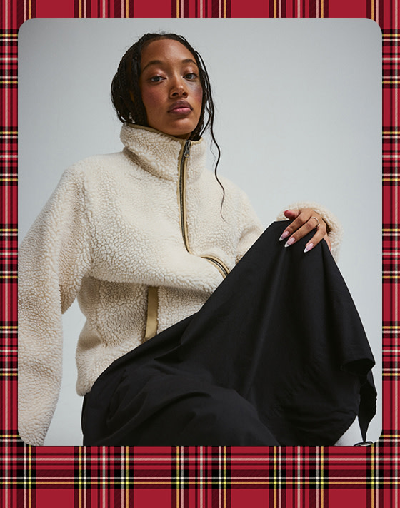 A photograph surrounded by a plaid holiday border of a young woman wearing a white High-Pile fleece and a black Francesca Full Skirt.