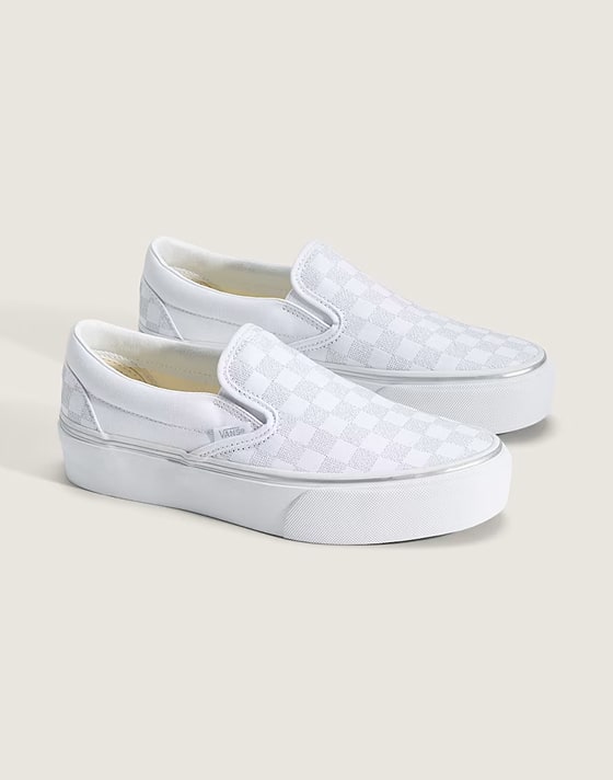 Une paire de Classic Slip-On Platform à motif damier argenté scintillant et blanc dans un studio photo.