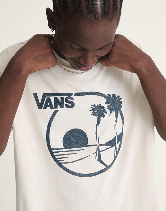 Close-up of a young man testing the fit of his white Vans tee with an archival print in a photography studio.