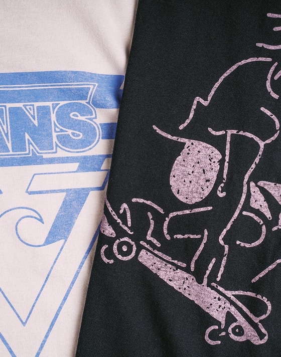 Close-up of two white Vans tees with vintage graphics laid out on top of each other.