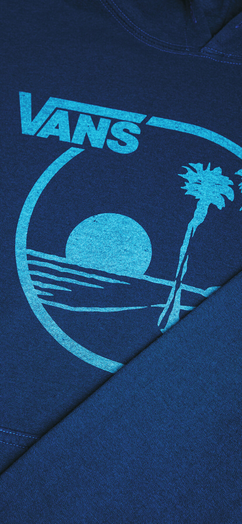 Close-up on an archival Vans graphic of a sun setting over the ocean with palm trees on a blue shirt.