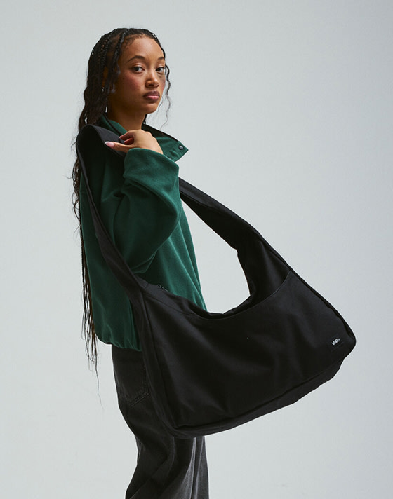 A young woman walking with a black bag and a green pullover in a photography studio.
