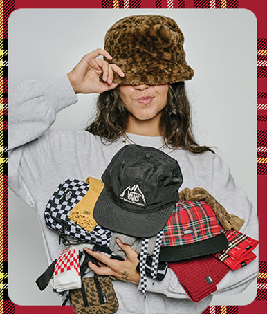 A young woman poses in a photography studio wearing a leopard print bucket hat and holding various Vans socks and hats.