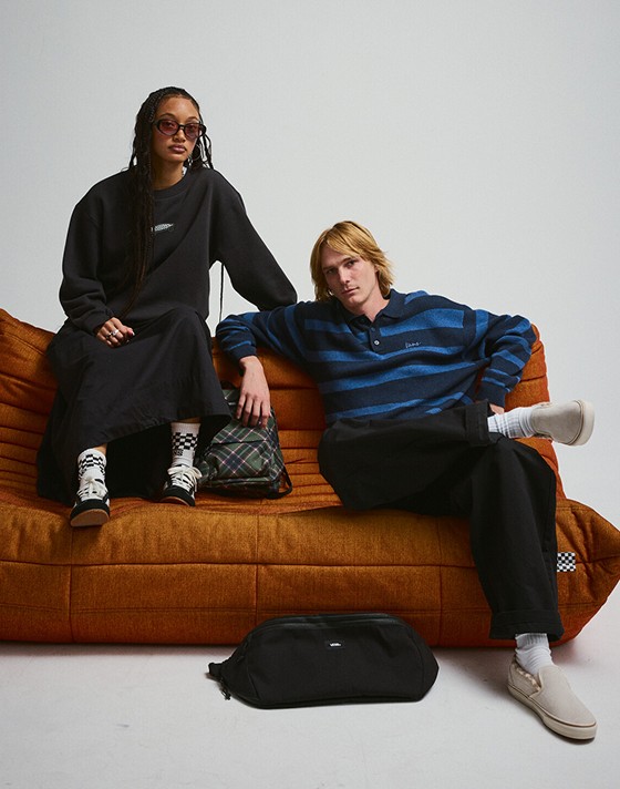 A young man and woman sit on an orange sofa in Vans shoes and clothes in a photography studio.