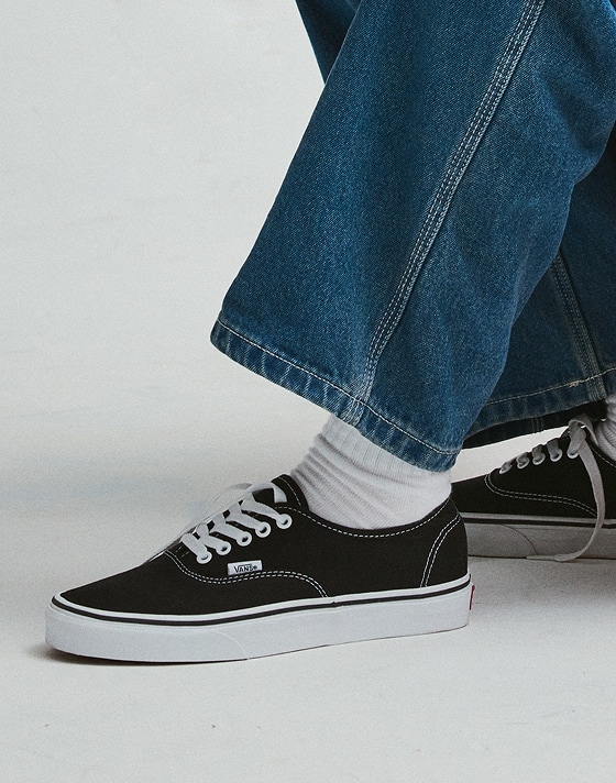 Close-up on someone wearing the black and white Authentic with blue jeans and white crew socks.