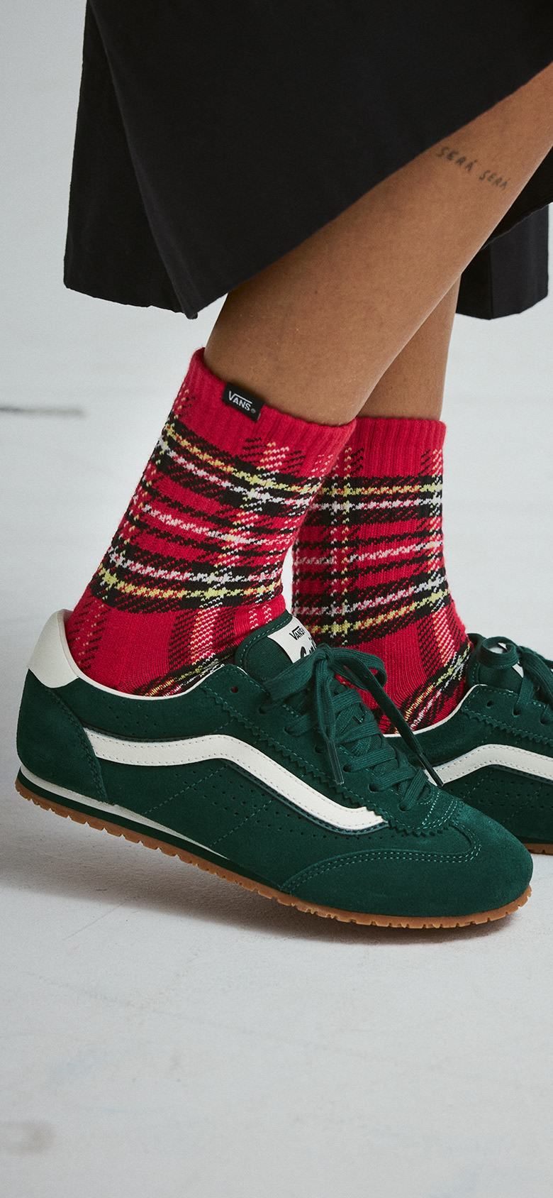 A young woman poses in a photography studio wearing green Super Lowpro, red plaid crew socks, and the black Francesca Full Skirt.