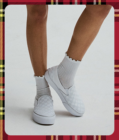 A photograph surrounded by a plaid holiday border of a woman wearing the white and gray Classic Slip-On Platform Checkerboard with white frill socks.