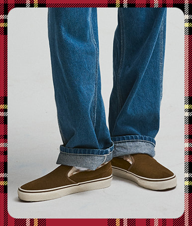 A photograph surrounded by a red plaid holiday border of the high pile Classic Slip-On paired with white crew socks and blue jeans.