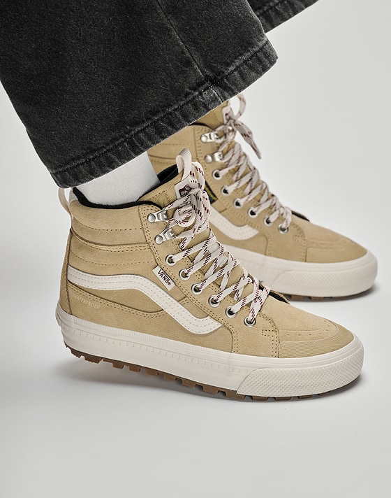 Close-up of a man sitting on a box wearing tan Sk8-Hi Insulated boots with black jeans in a photography studio.