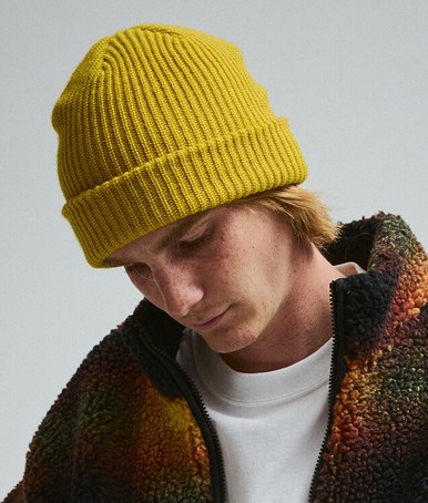 A young man wearing a High Pile Fleece Jacket and a yellow beanie in a photography studio.