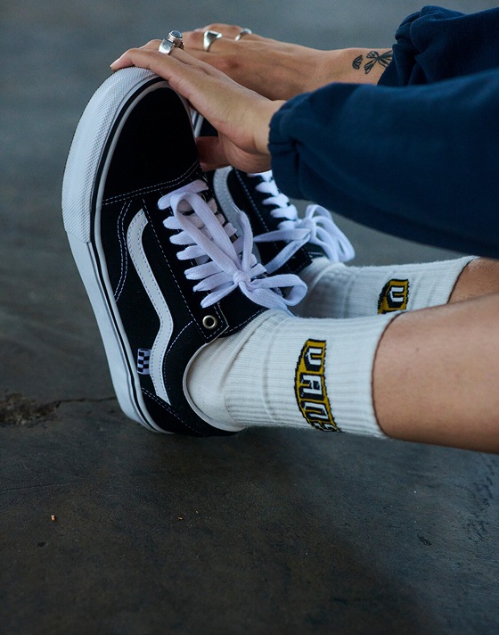 A person stretches and touches their toes in white Vans crew socks and black and white Old Skool.