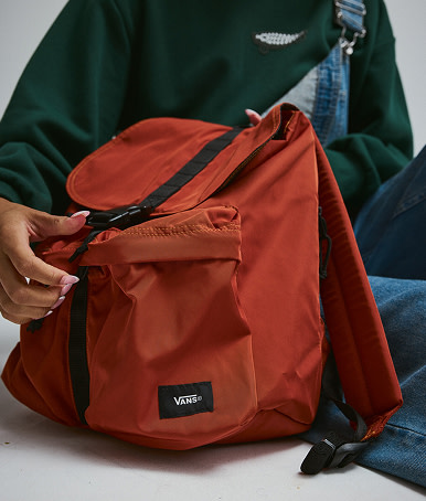 A close-up of someone holding the black Scatter Backpack against the blue denim Sirelle overalls in a photography studio.