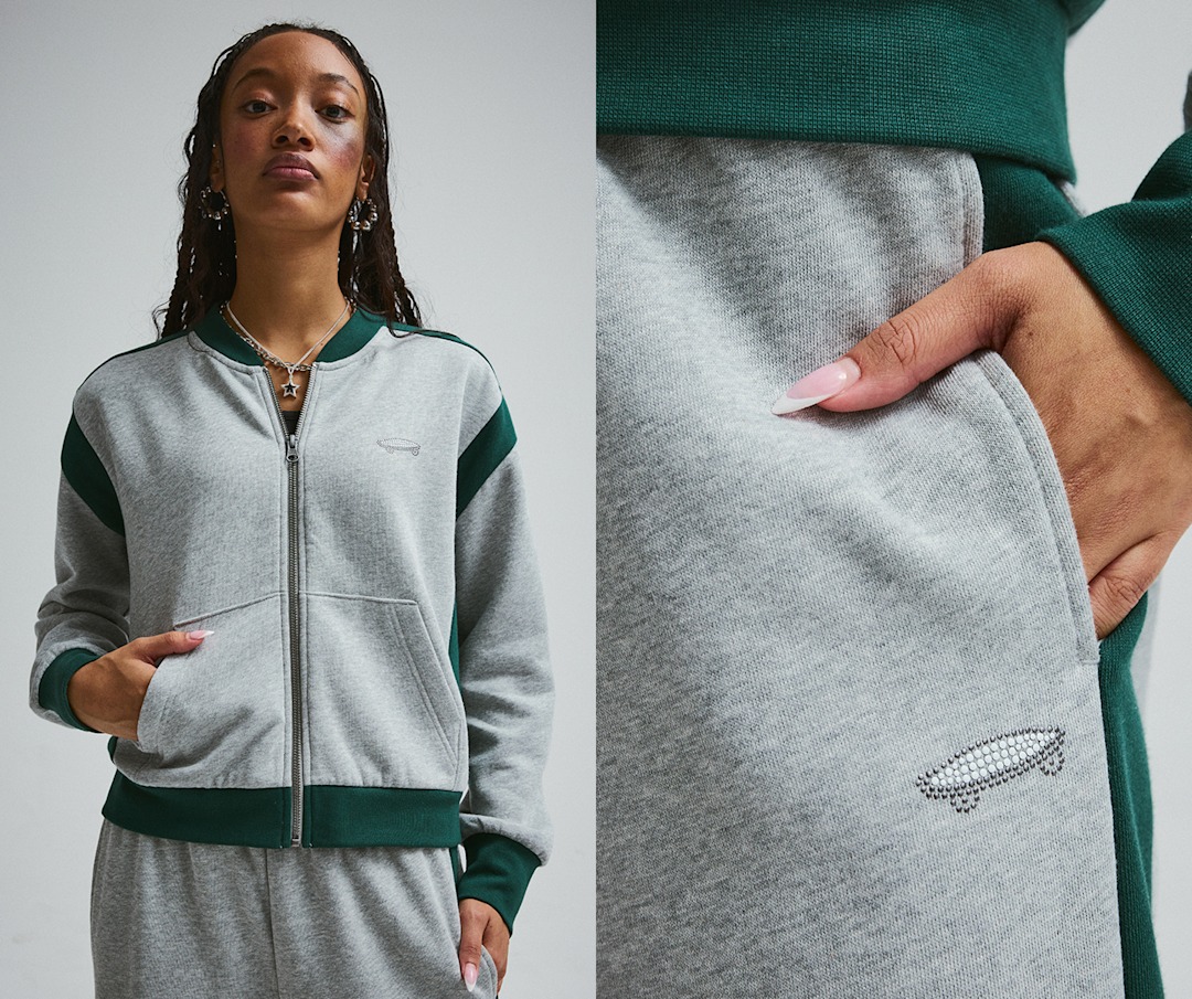 A young woman poses in a photography studio in an emerald and gray sweat bomber and sweat pants.