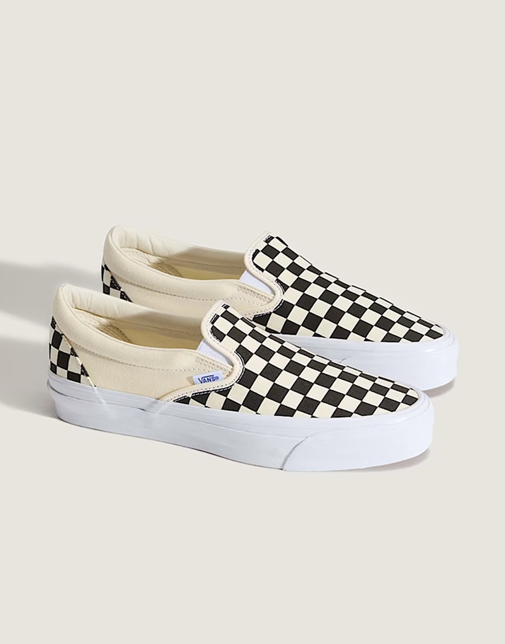 A pair of black and white Premium Classic Slip-On Checkerboard shoes in a photography studio.