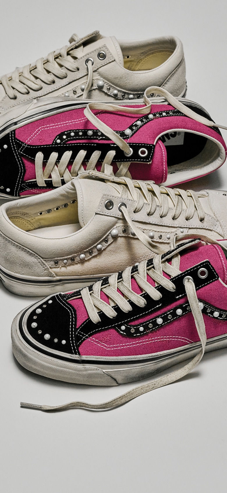 The white colorway and the magenta and black colorway of the Premium Old Skool 36 Pearlized shoes lie on the floor of a photography studio.