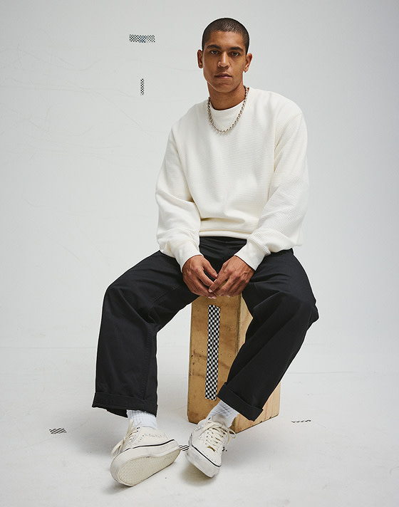 A young man sits on a box wearing white Premium Old Skool 36 Pearlized shoes.