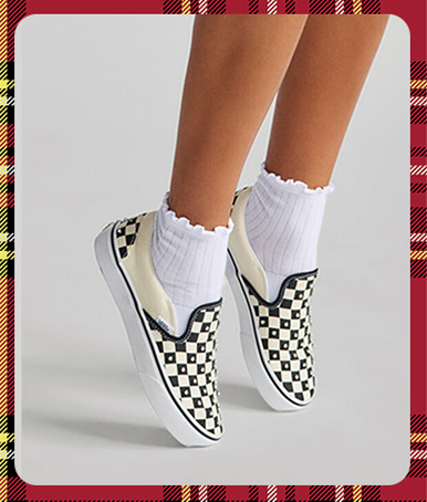 A woman stands on her toes in the Premium Classic Slip-On Pearlized with white frilly socks in a photography studio.