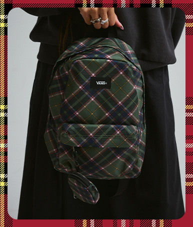 A woman holds a pine forest Old Skool Mini Backpack against a black outfit.