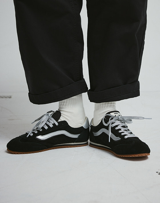 Close-up of someone wearing black and silver Super Lowpro with white crew socks and black jeans in a photography studio.