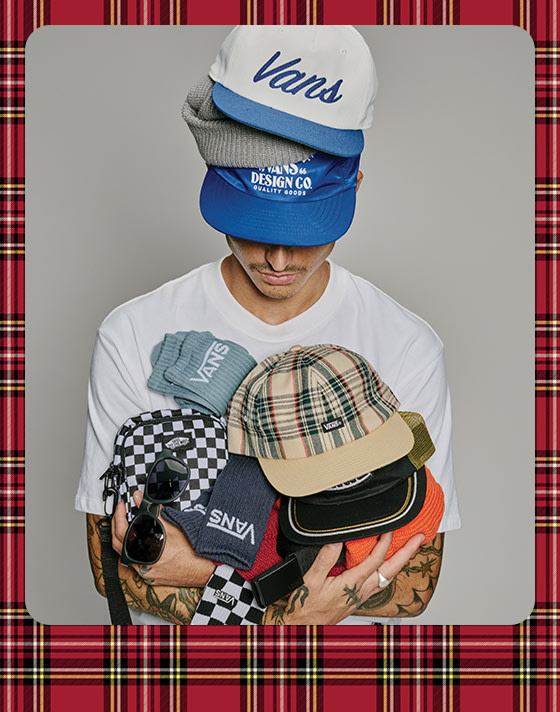 A photograph surrounded by a red plaid holiday border of a young man wearing Vans hats stacked on each other and holding various Vans socks and hats.