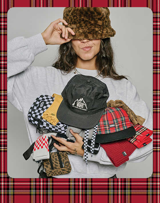 A photograph surrounded by a red plaid holiday border of a young woman wearing a leopard print bucket hat and holding various Vans socks and hats.