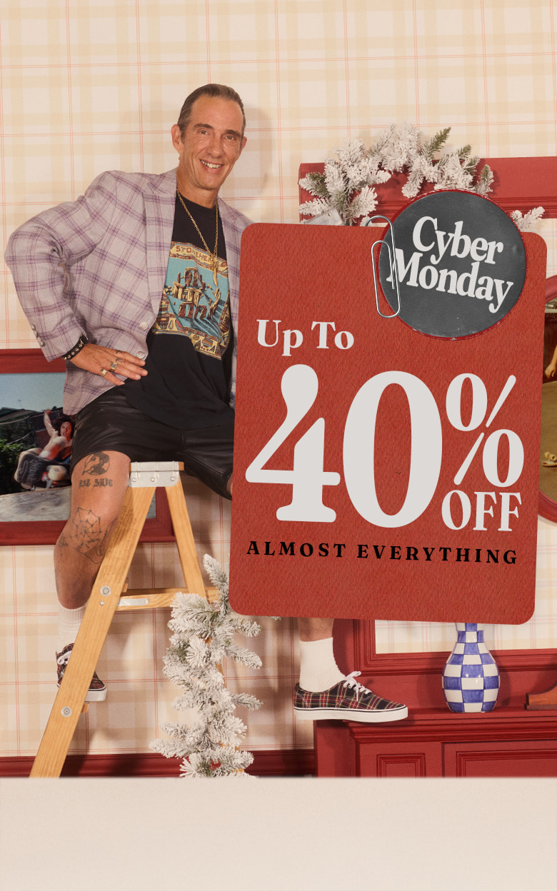 A photo of artist Cali DeWitt sitting on a ladder in a living room under a card that says up to 40% off almost everything for Black Friday.