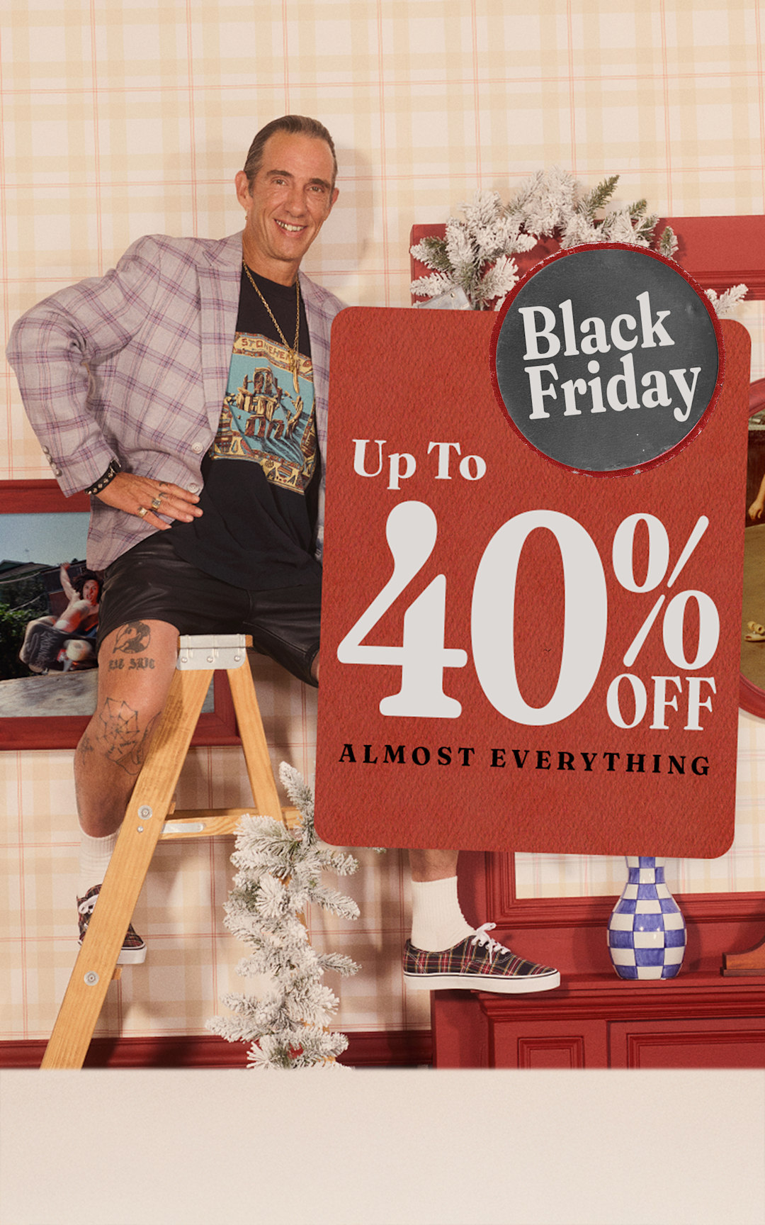 A photo of artist Cali DeWitt sitting on a ladder in a living room under a card that says up to 40% off almost everything for Black Friday.