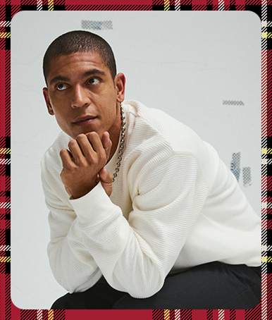 A plaid holiday border around an image of a young man wearing a white Vans thermal long-sleeve shirt in a photography studio.