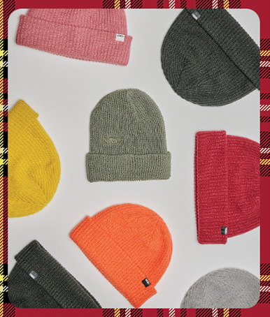 A plaid holiday border around an image of a variety of Vans beanies in different colors on the floor of a photography studio.
