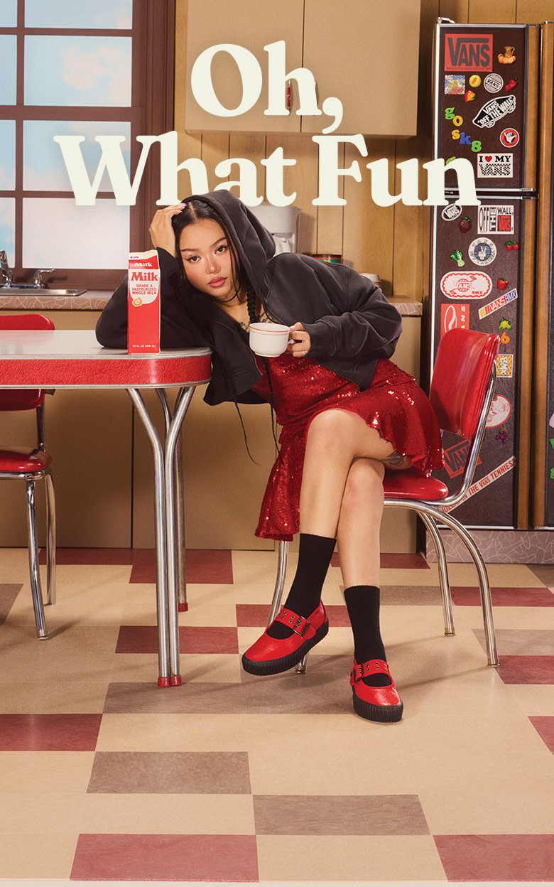 Influencer Bella Poarch sits at a kitchen table wearing the racing red Mary Jane Creeper next to a carton of milk on a sitcom set.