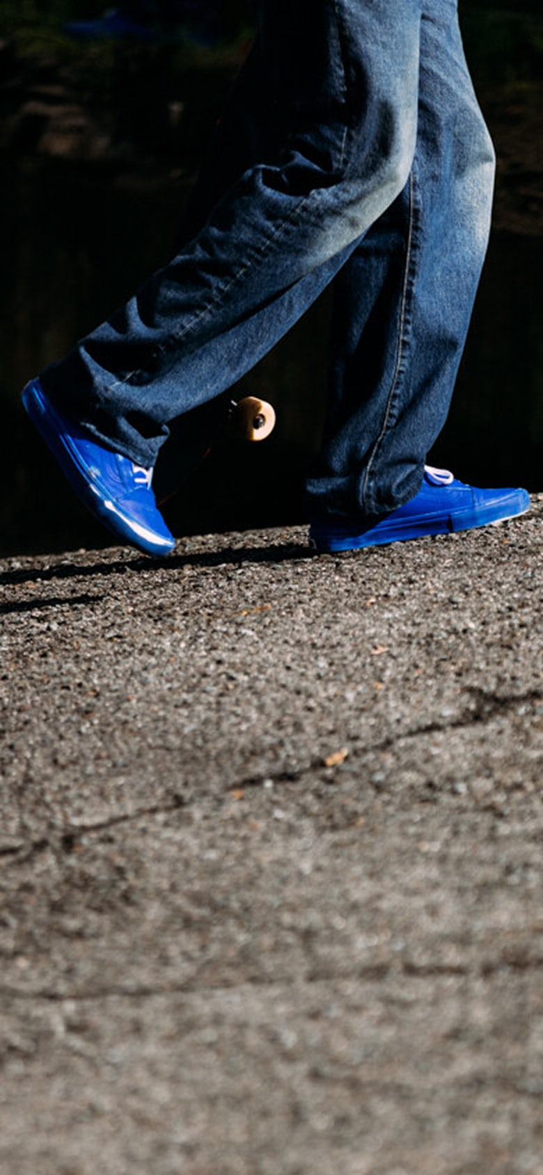 A waist-down shot of a skater carrying his board and wearing blue Skate Old Skool by 2 Riser Pads.