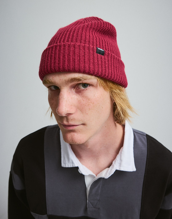 Close-up on a young man wearing a pink Core Basic Cuff Beanie and a gray and black Grant Checkerboard Rugby shirt in a photography studio.