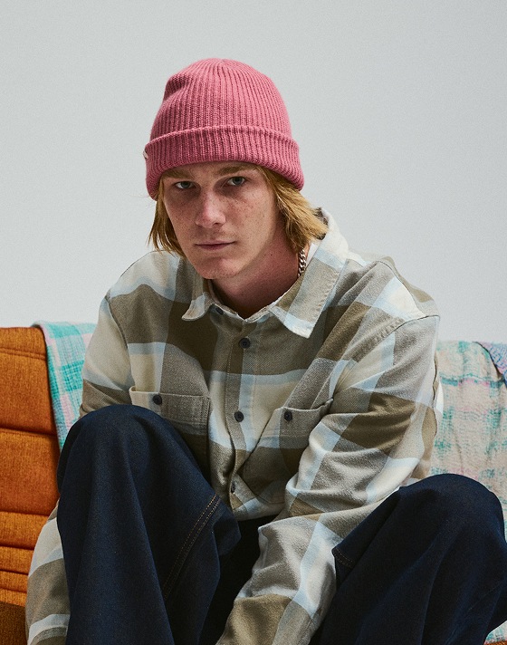 Man wearing a pink Vans Core Basic Cuff Beanie with a Vans Larkspur Flannel Shirt on, looking directly at the camera in a photography studio.