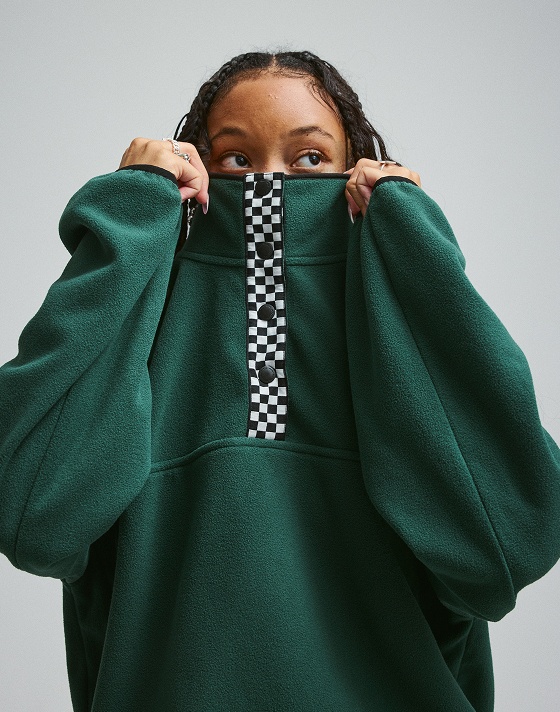 A young woman pulls an emerald Polar Sweatshirt over half of her face in a photography studio.
