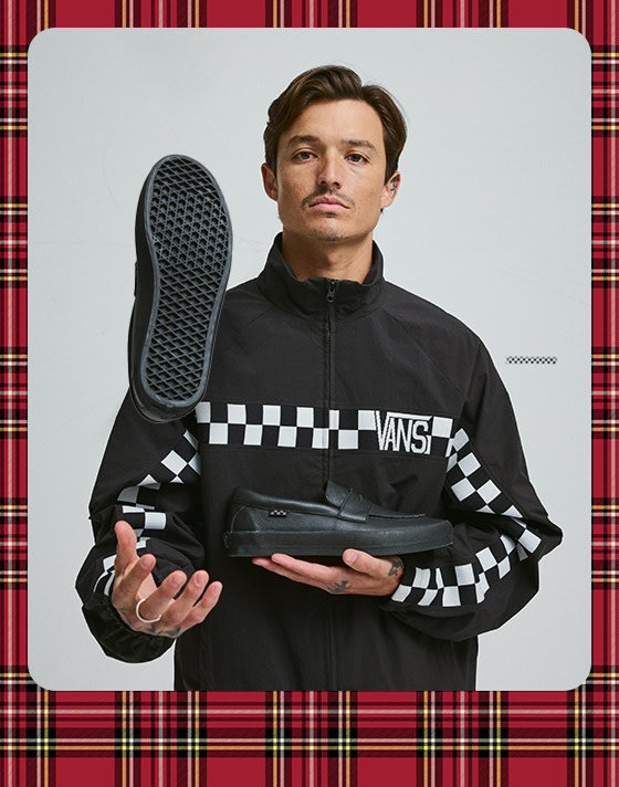 Un jeune homme portant un manteau Ronnie Track noir lançant un mocassin Skate noir dans les airs.