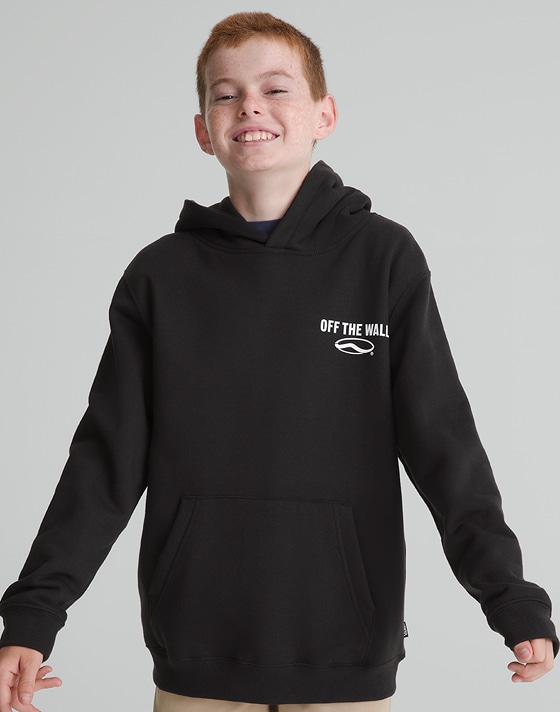 A young boy poses in a photography studio with his arms out in a black Vans pullover hoodie.
