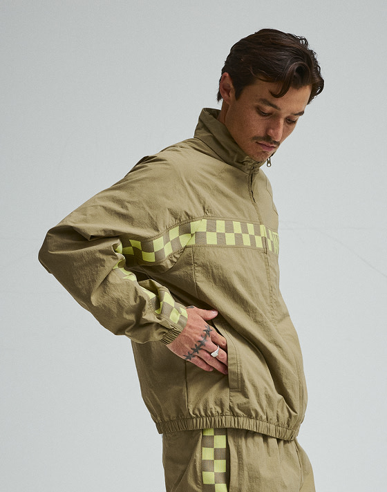 A young man puts his hand in the pockets of the yellow and brown Ronnie Track Jacket in a photography studio.