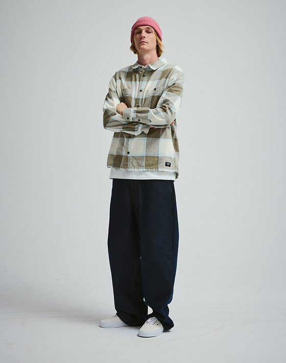 A young man poses in a photography studio wearing a turtledove white Larkspur Flannel Shirt and white Authentic Knit shoes.