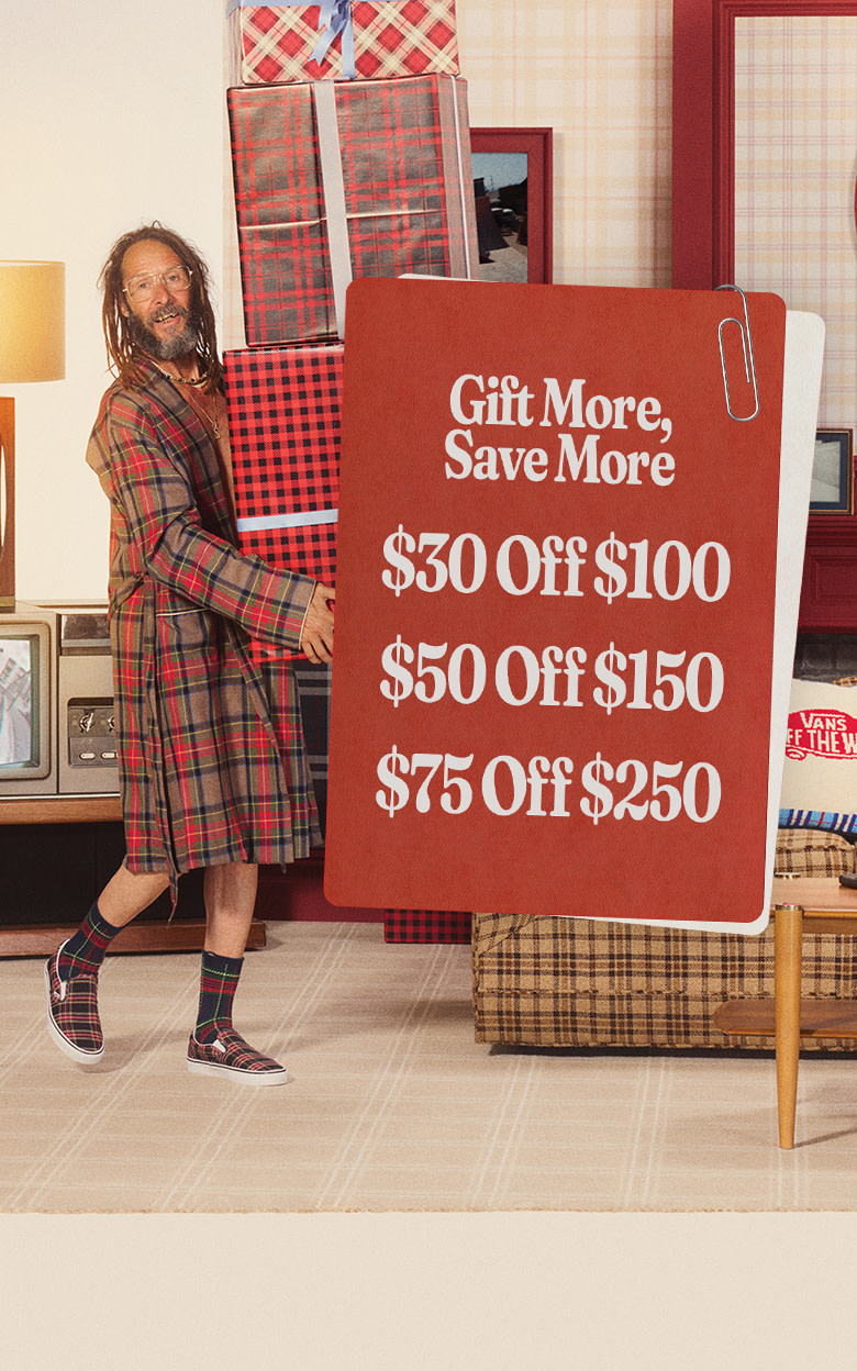 Skate Legend Tony Alva carries a stack of presents wearing plaid Premium Classic Slip-On and a plaid robe on the set of a sitcom.