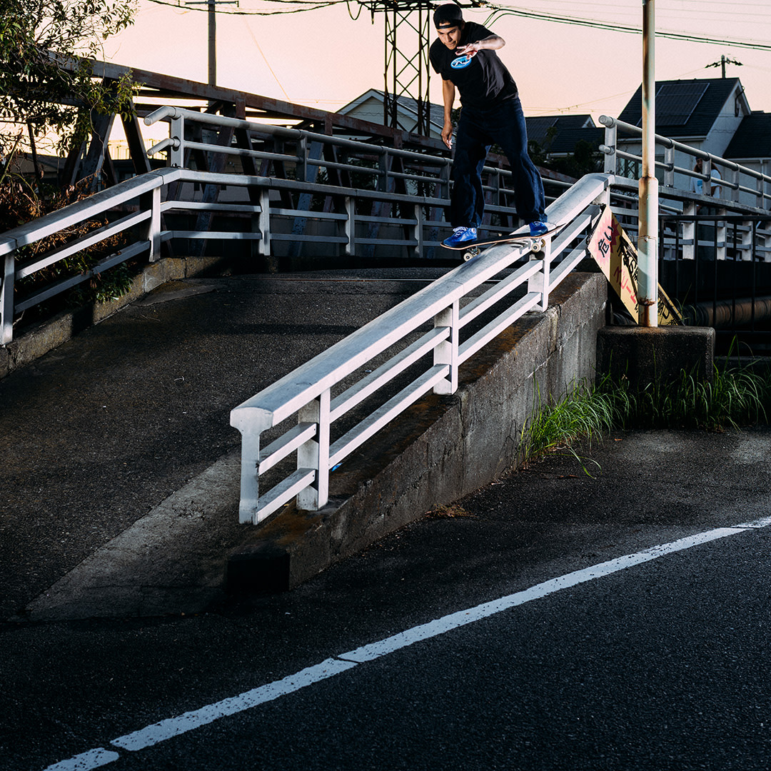 Skateboarder boardslides a white handrail on a street bridge.