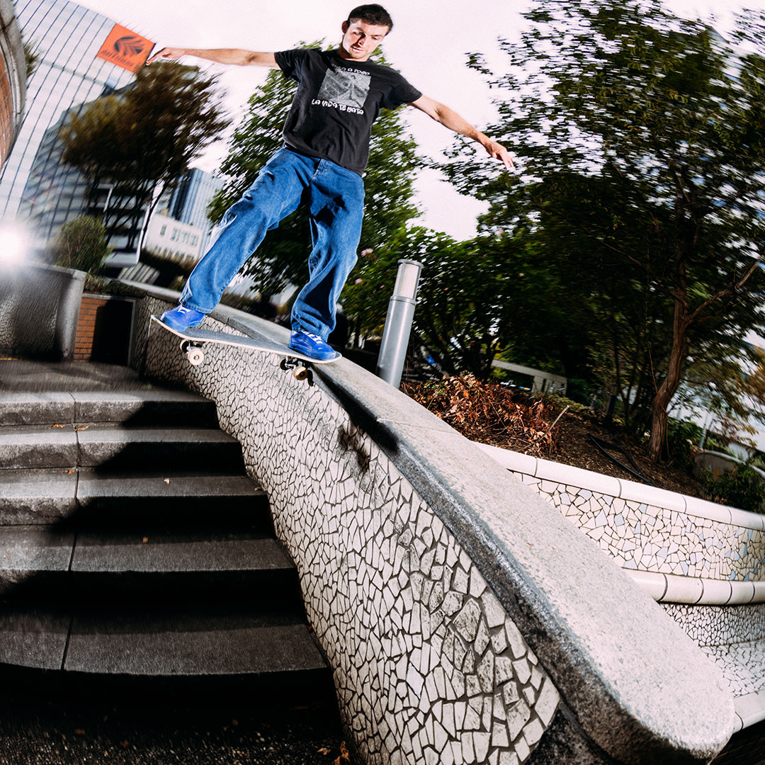 Skateboarder grinding a curved ledge above a stair set in an urban plaza, captured mid-movement with motion blur.