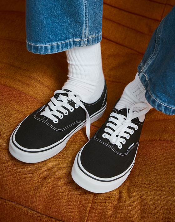 Black and white Authentic paired with white socks and blue jeans on an orange sofa.